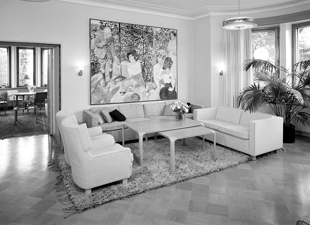 Black and white photo of living room with two couches, two chairs, a large painting, and a large plant