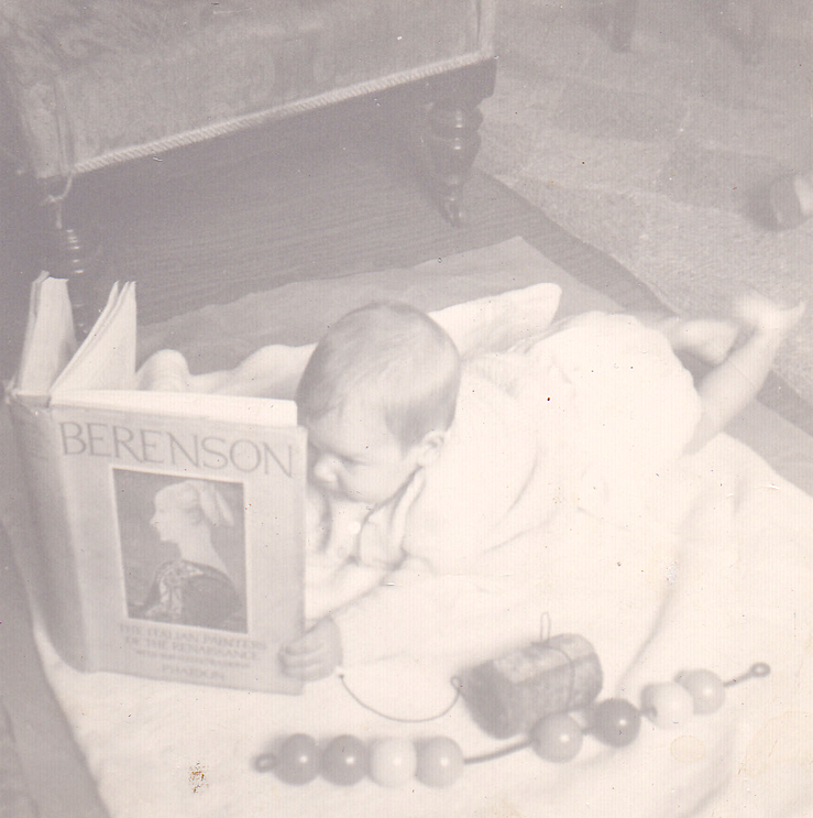 Black and white photograph of Frances Anderton as a baby holding up a book on the floor