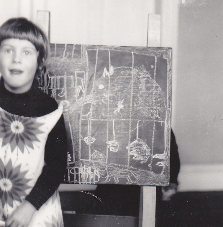 Frances Anderton as a little girl standing in front of drawings on a blackboard