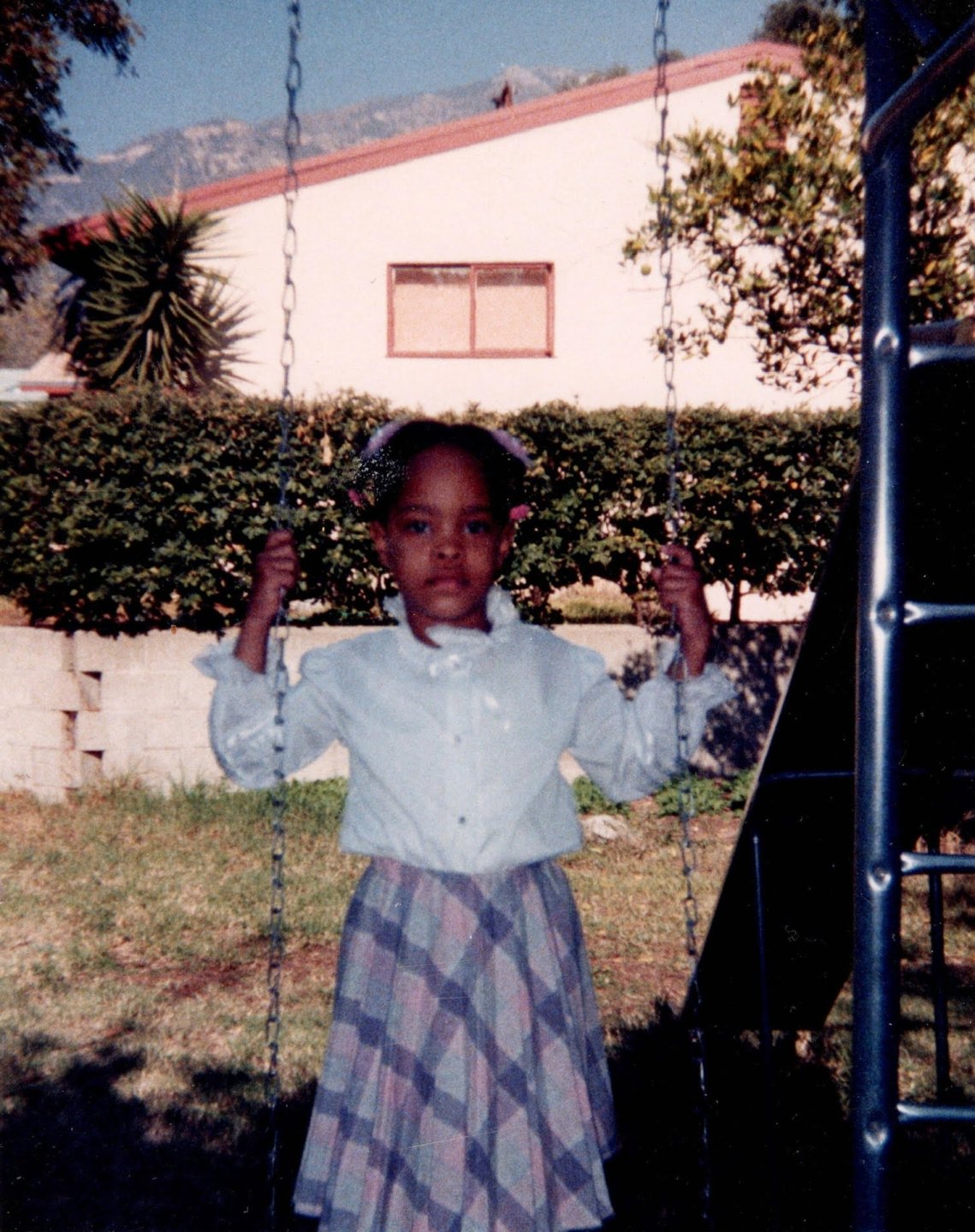 Childhood photo of artist Kenturah Davis standing on a swing in her backyard