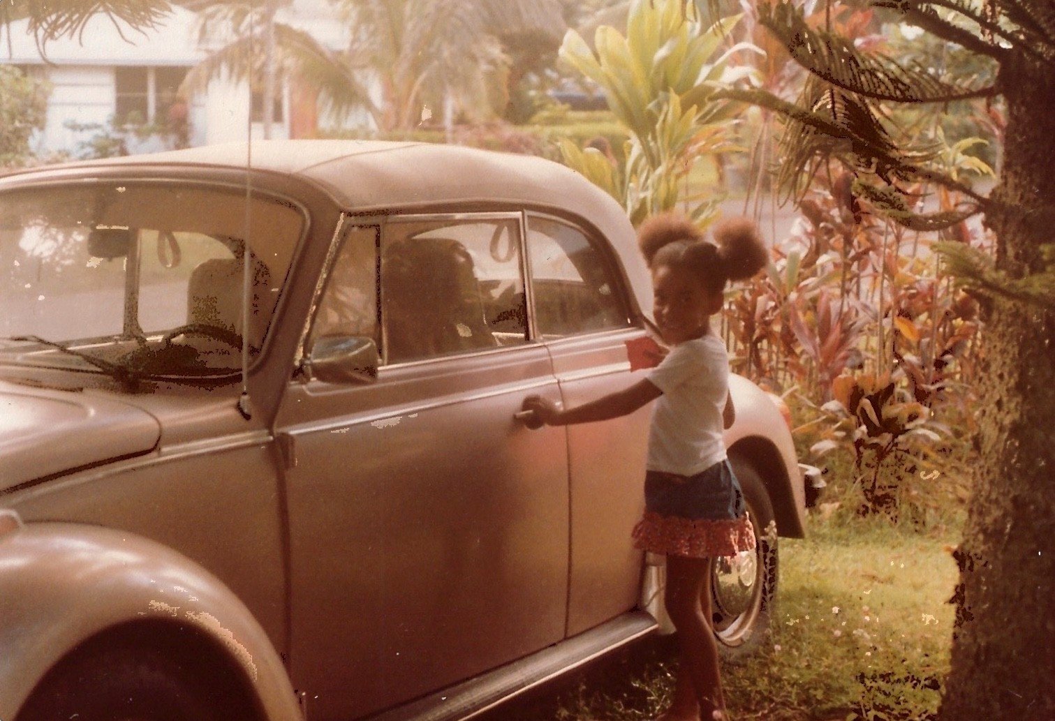 Little girl standing outside with her hand on the handle of a vintage car in Hawaii