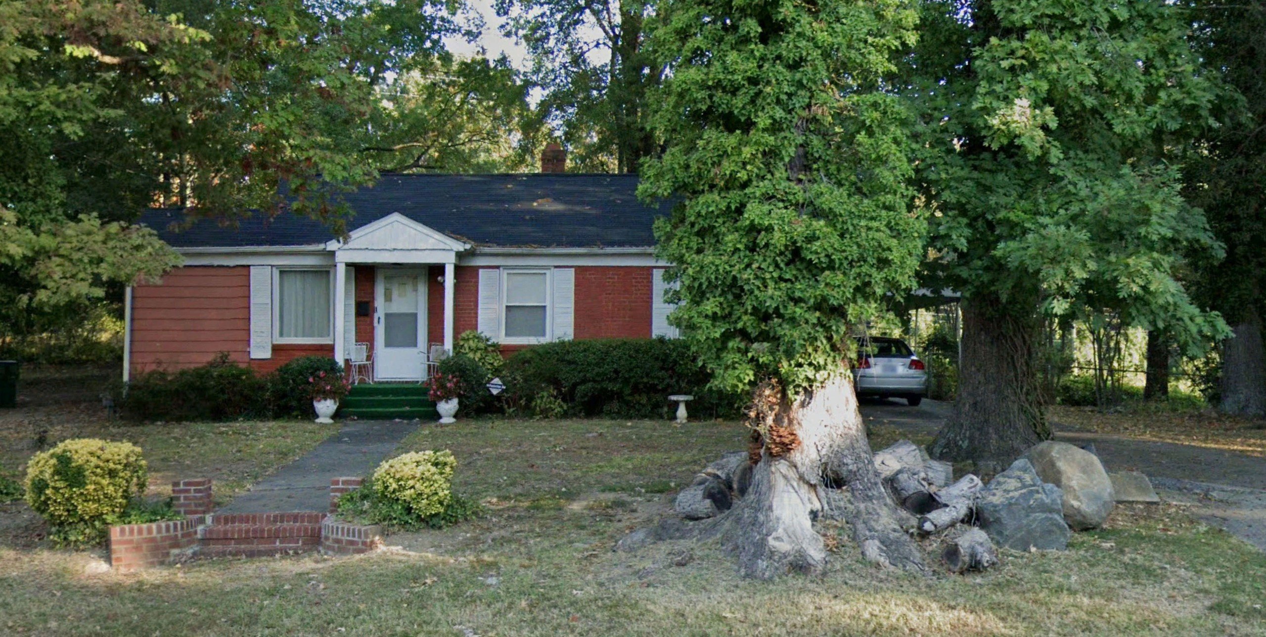 Exterior view of red brick house in Charlotte, North Carolina, with black roof and two trees out front