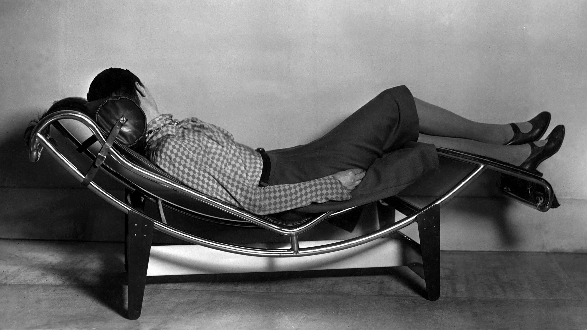 Black and white photo of Charlotte Perriand on lounge chair facing away from camera