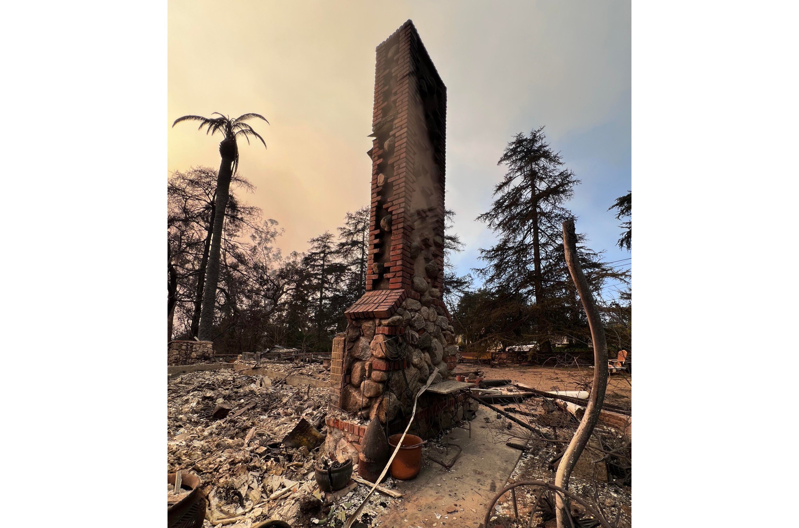 Charred brick and stone chimney standing over the remnants of a burned-down house in Altadena, California after the Eaton Fire