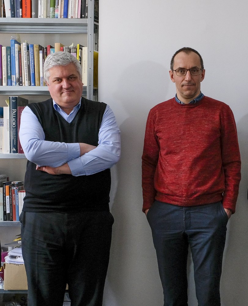 Portrait shot of Pier Vittorio Aureli and Martino Tattara standing side-by-side in front of book case.