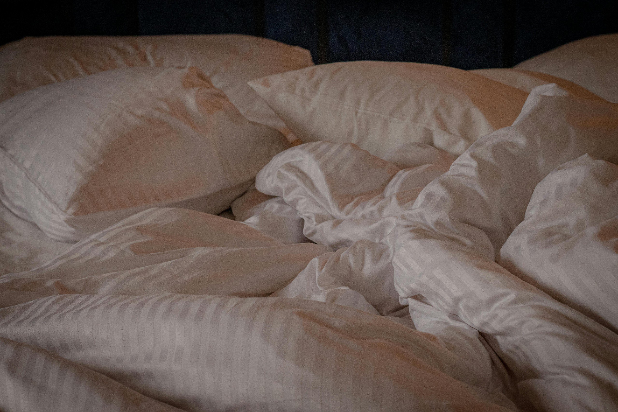 Rumpled white blanket and pillows on bed