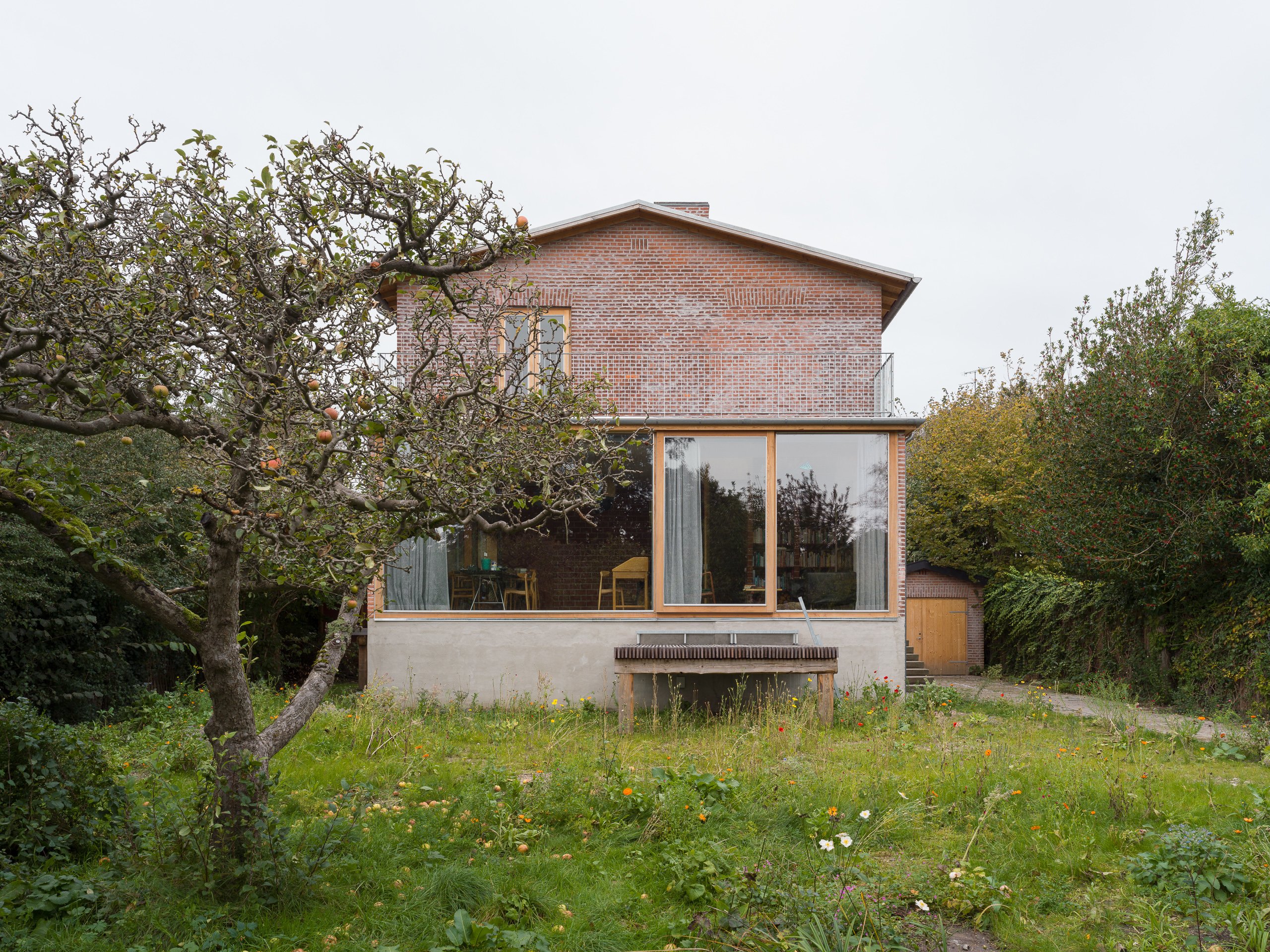 Wide shot of the side of art historian and curator Marianne Krogh's house in a green field with sliding glass doors on the first level.