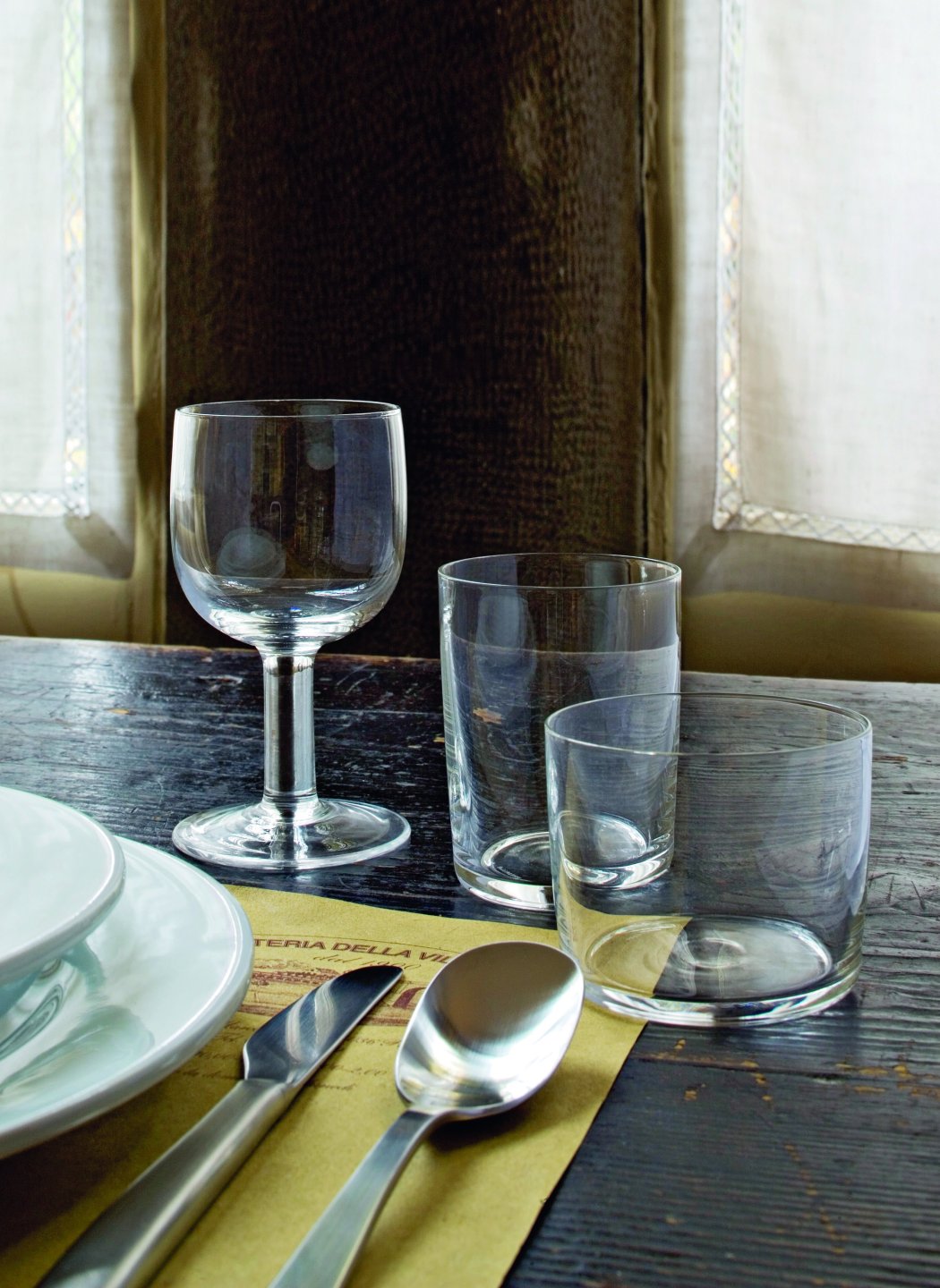 Three glasses on a set table, one wine glass with a thick stem and two cylindrical water glasses, designed by Jasper Morrison