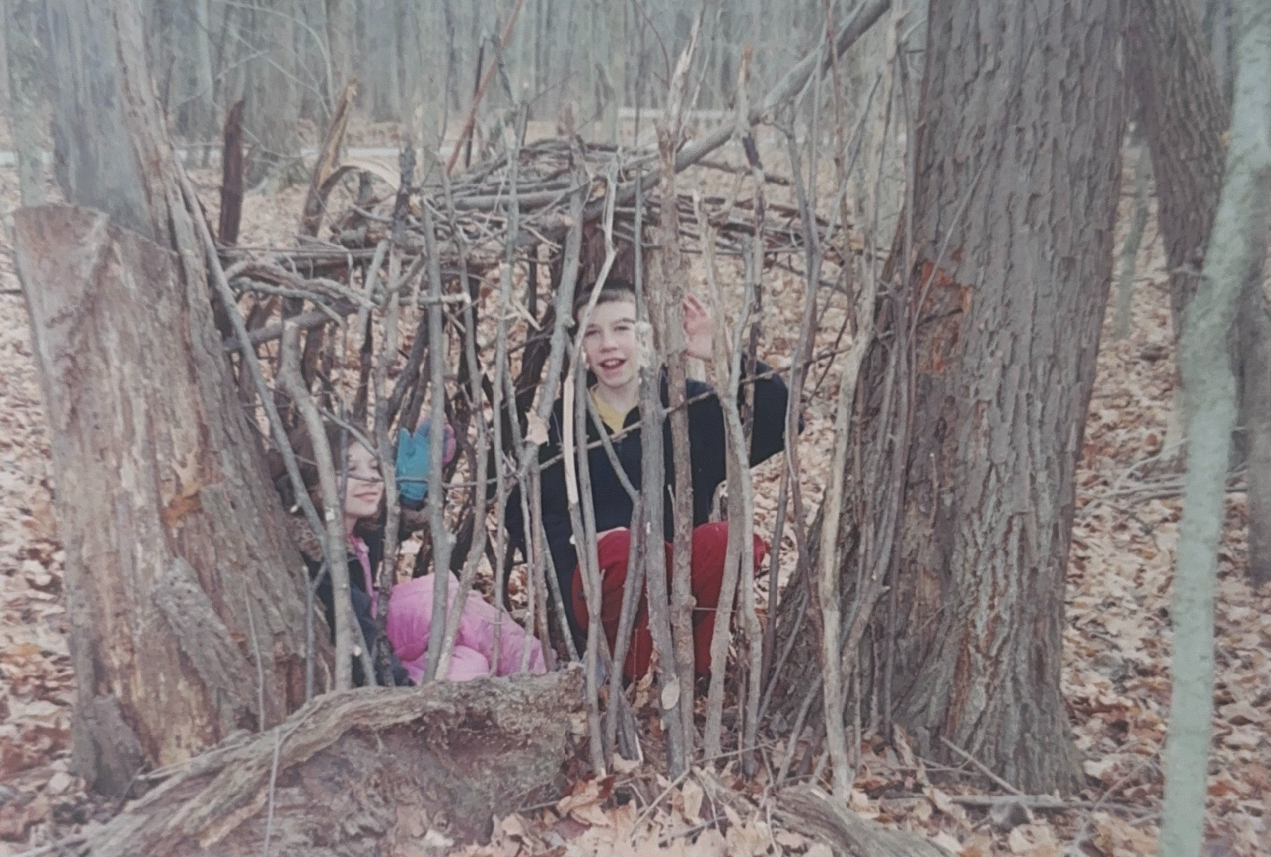 A little girl and boy bulding a fort in the woods.