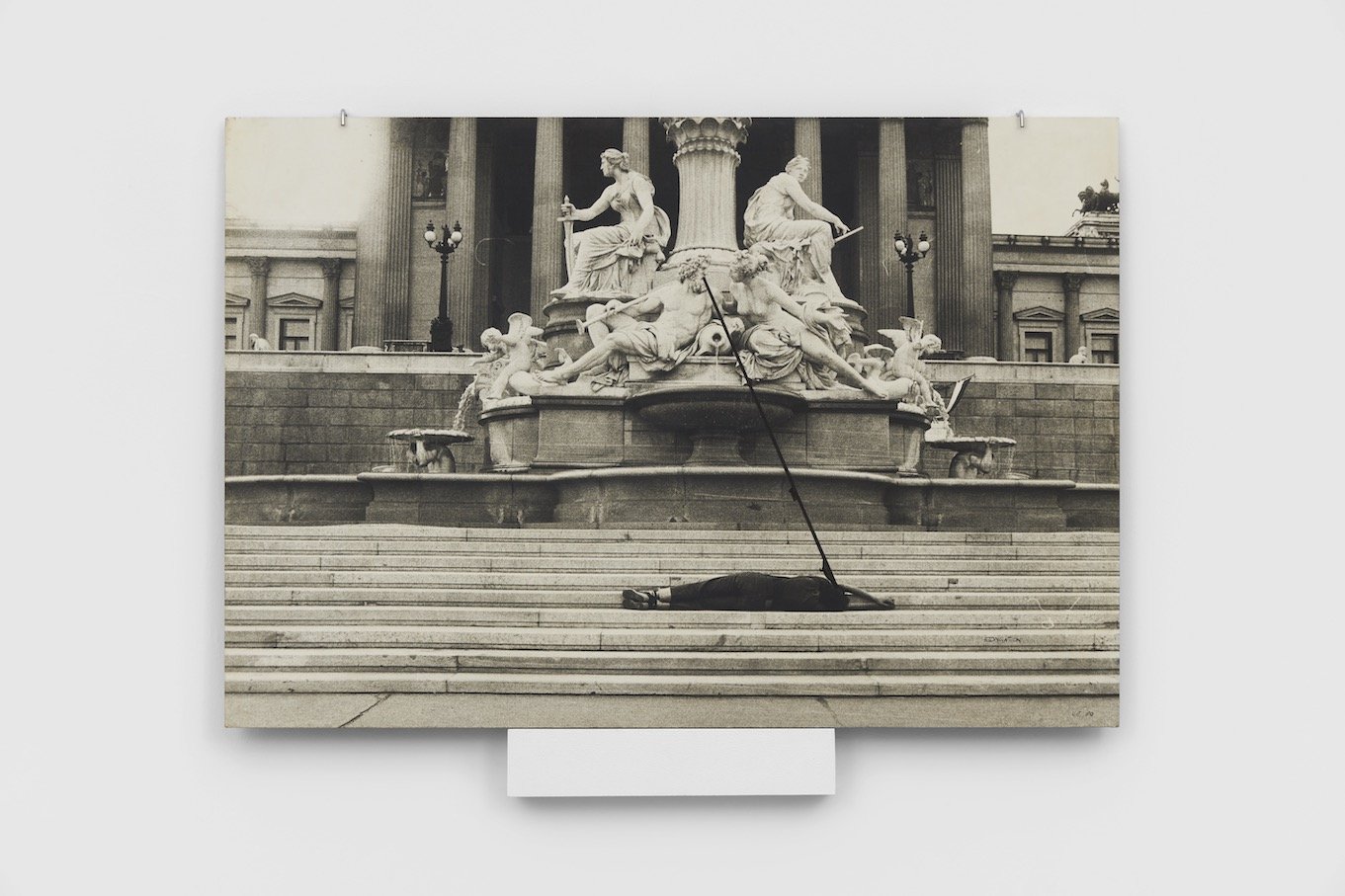 Black and white image of woman lying down on the steps leading up to an ancient statue, facing her face to that of a man in the statuetoward the statue with a black line connecting